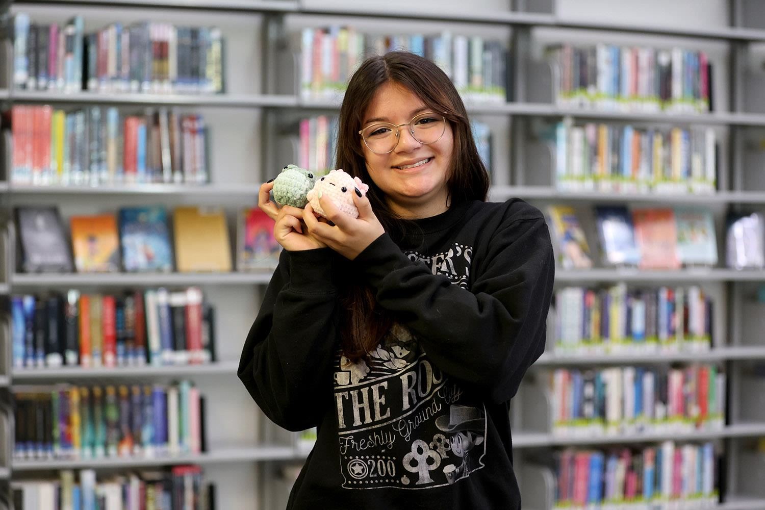 Esther holding two of her "Something Smol" chrochet characters and smiling in the GISH Media Center. 